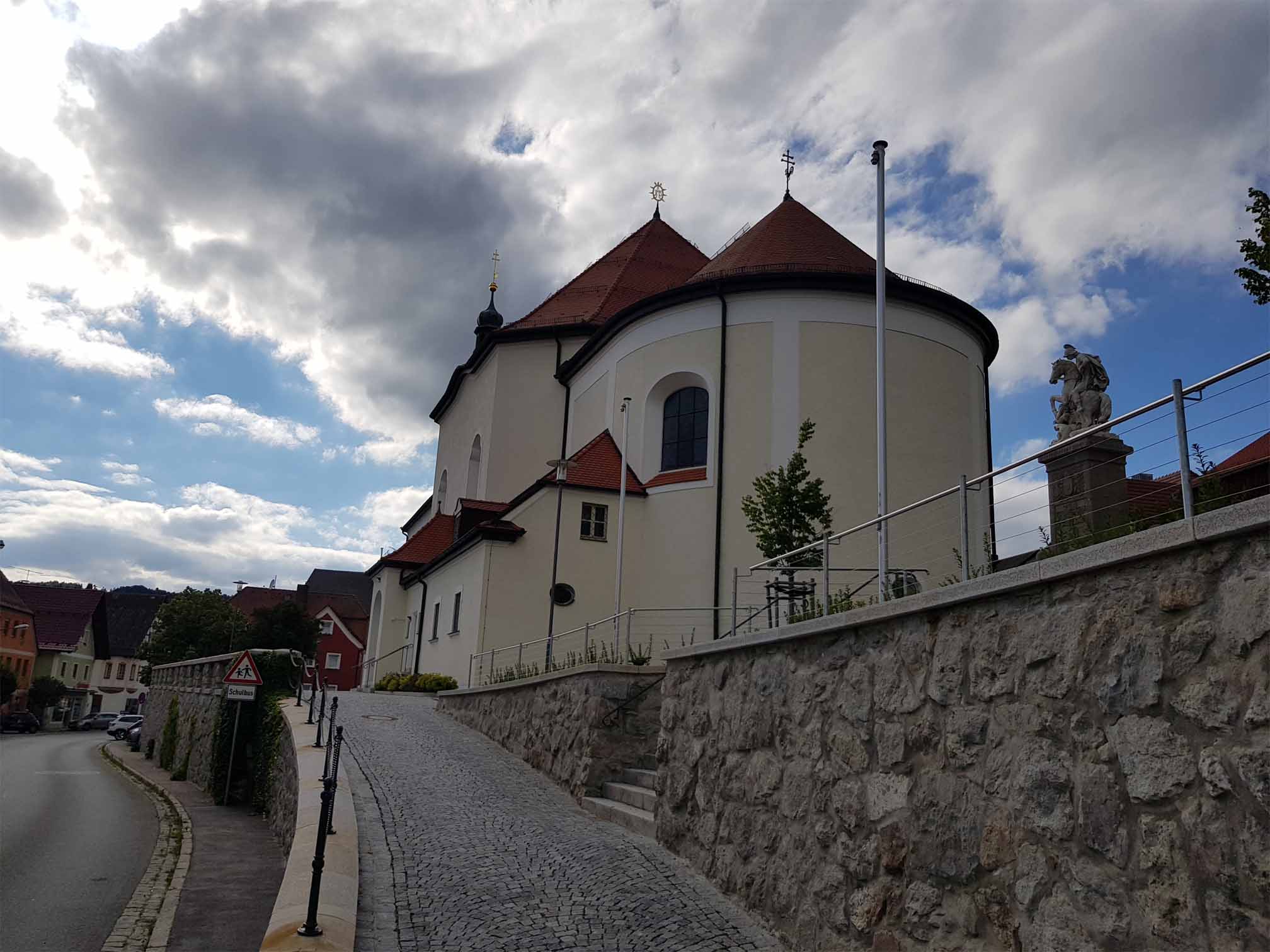 Eine weisse Kirche mit einem hohen Turm steht auf einem Huegel neben einer Strasse